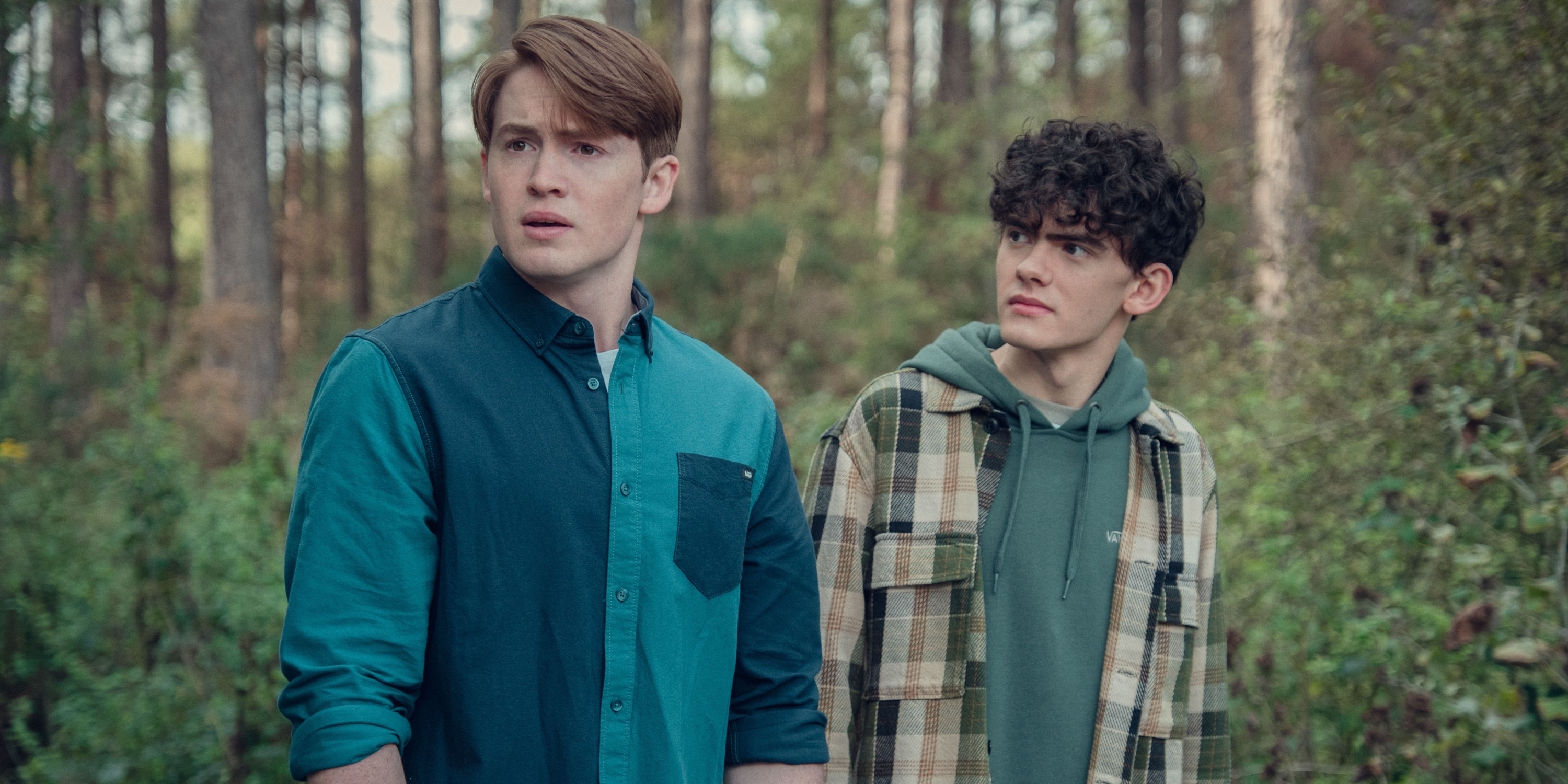 closeup of two teens standing in the woods, looking concerned