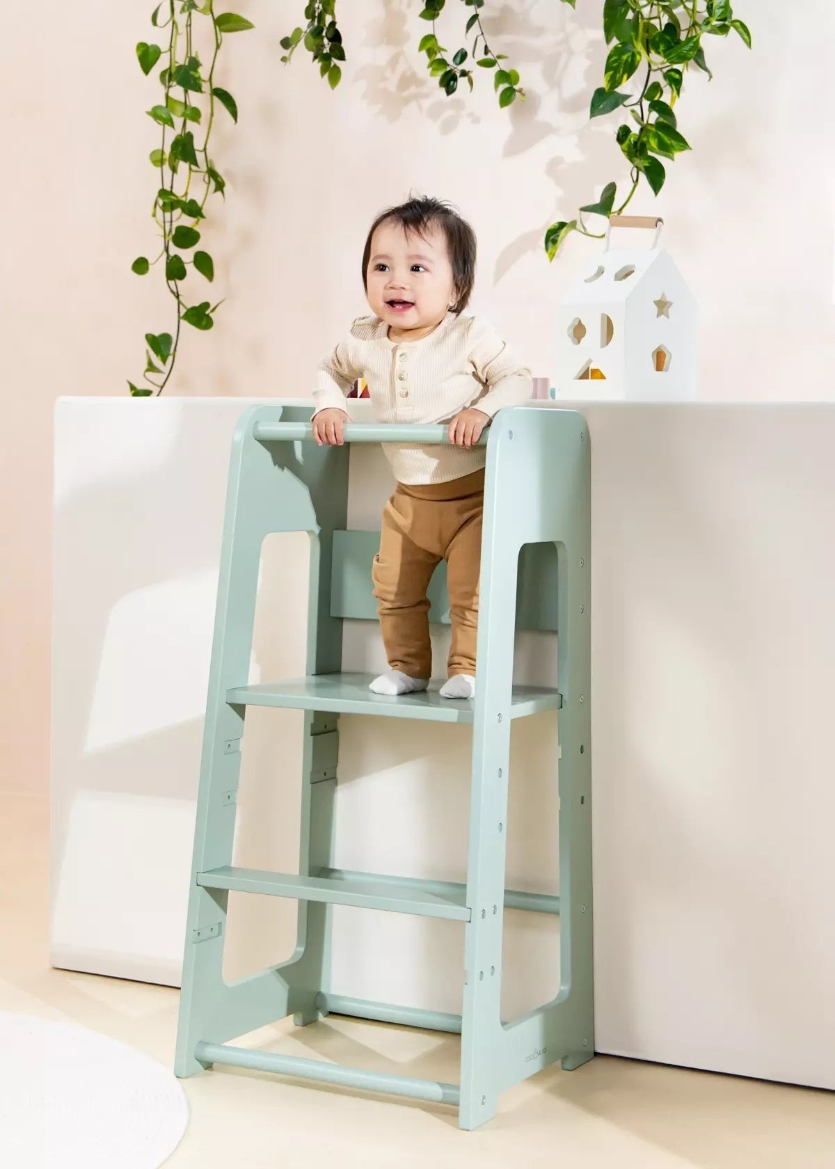 Toddler stands on a learning tower, reaching for a shelf, in a home environment