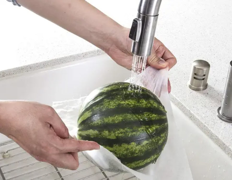 large watermelon being rinsed in kitchen sink and wiped with bamboo towels