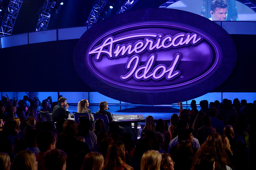 American Idol logo on stage with judges facing the audience, lights illuminating the setting