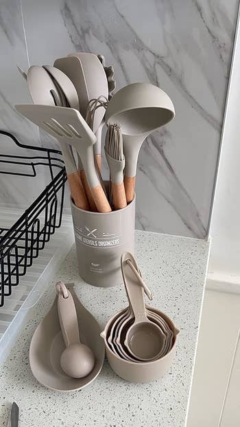 A reviewer's variety of kitchen utensils in a holder next to nesting measuring cups on a counter
