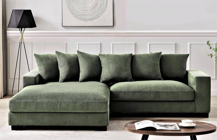 L-shaped green sofa with cushions in a living room, accompanied by a coffee table with a magazine on top