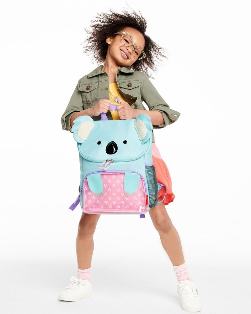 Model poses with a blue and pink koala backpack with front zip pocket and water bottle side pocket