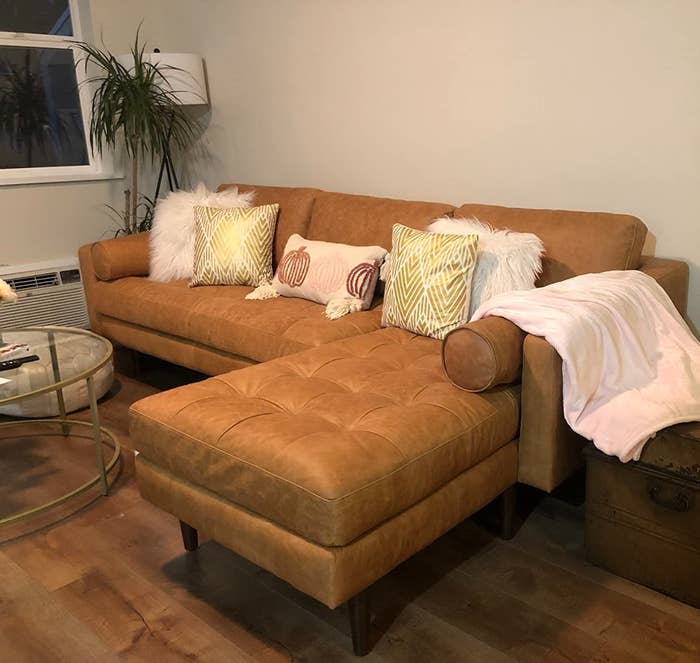 A sectional tan leather couch with decorative pillows and a throw blanket in a living room setting
