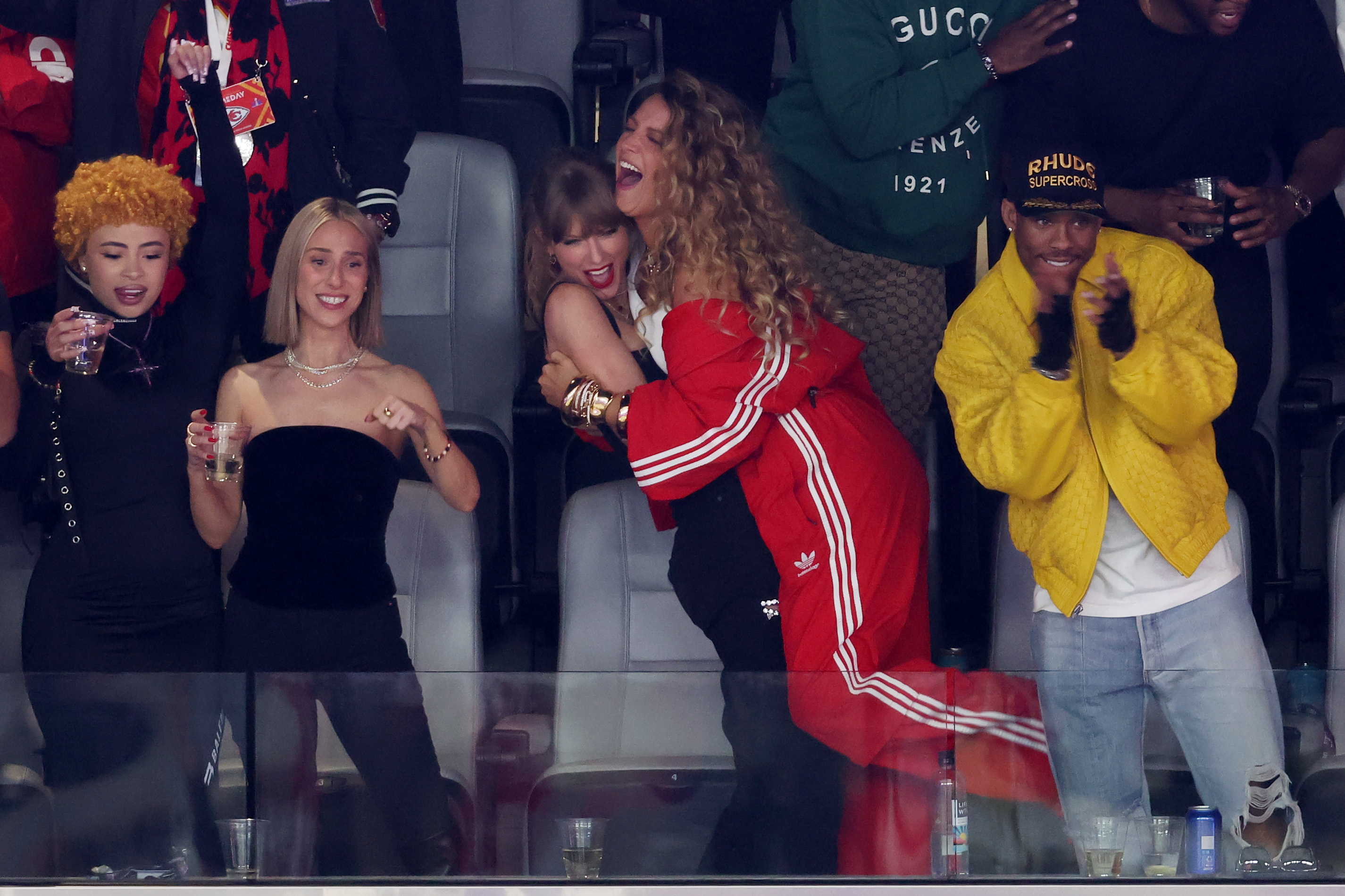 Group of people cheering at an event, including Blake in a red tracksuit hugging Taylor from behind