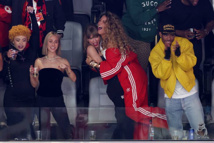 Group of people cheering at an event, one person in a red tracksuit hugging another from behind