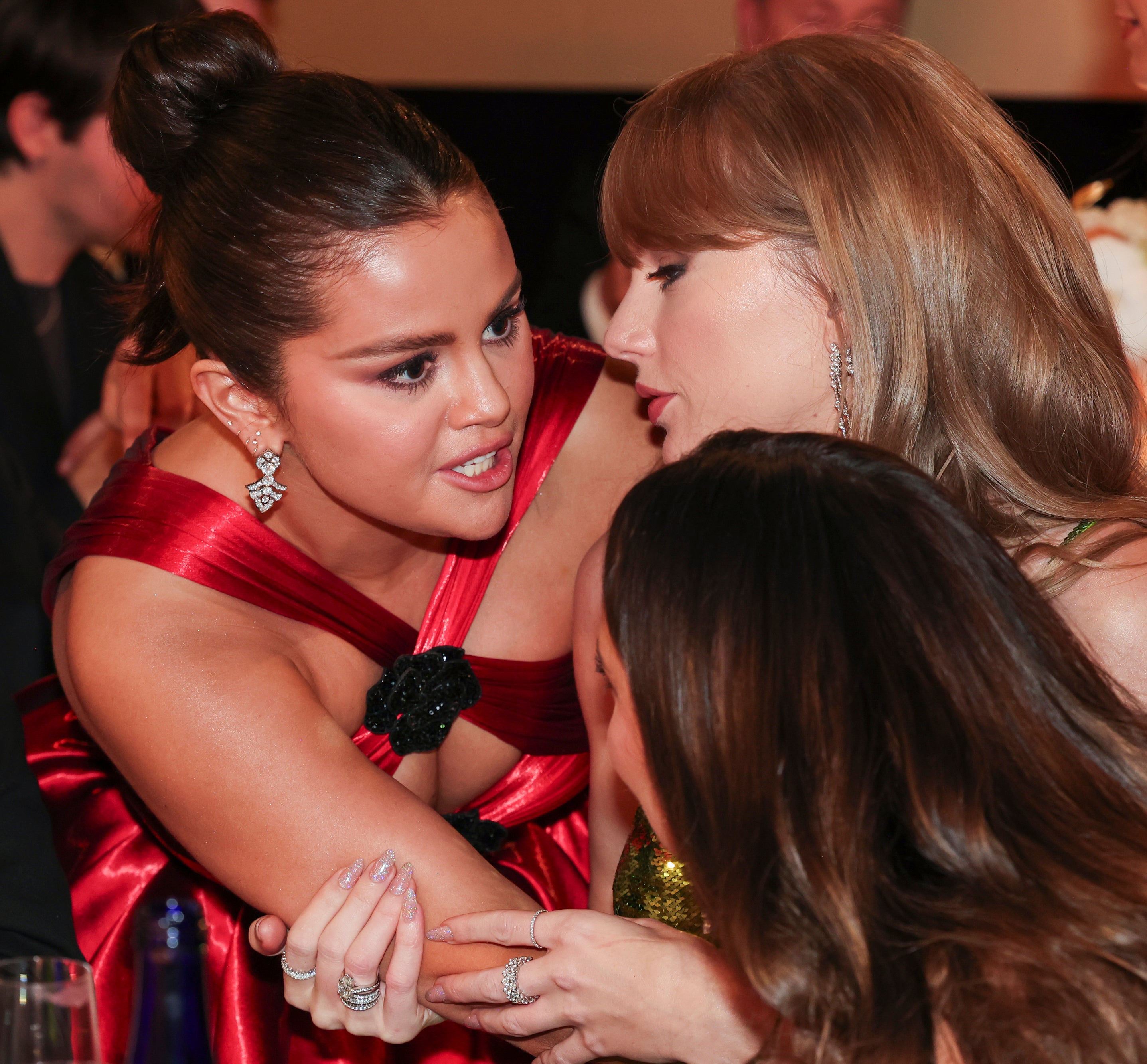 Two women in elegant attire leaning close, engaged in a private conversation at a formal event