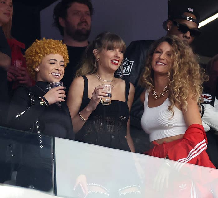 Ice Spice, Taylor, and Blake watching an event from a private box, one holding a beverage, sharing a joyful moment