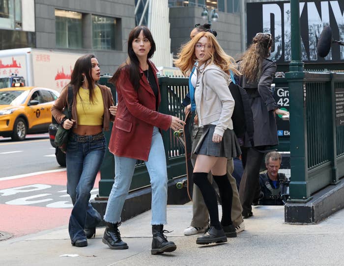 Four women walking on a city street, dressed in casual attire