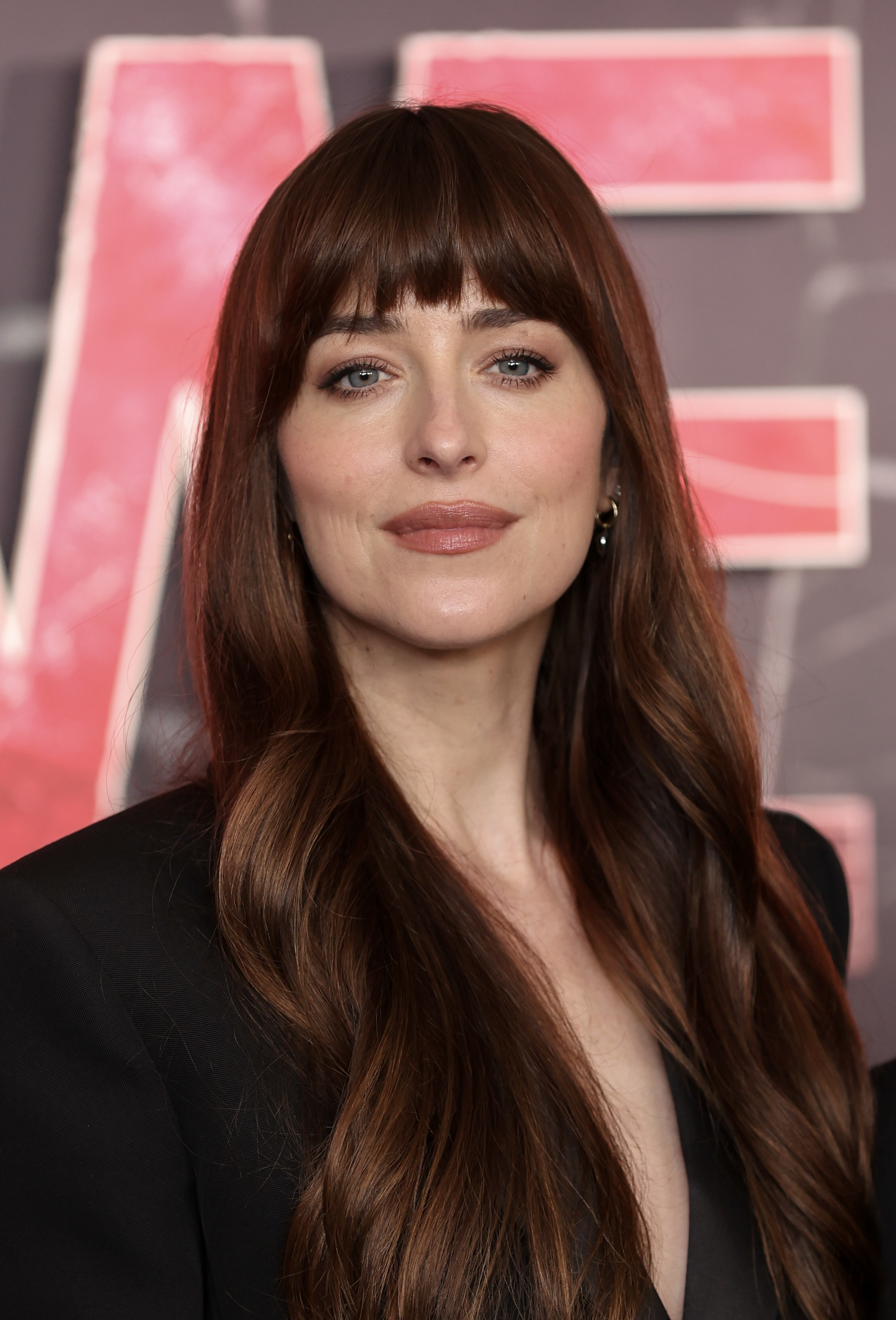 Close-up of Dakota in black blazer with long hair, smiling at a red carpet event