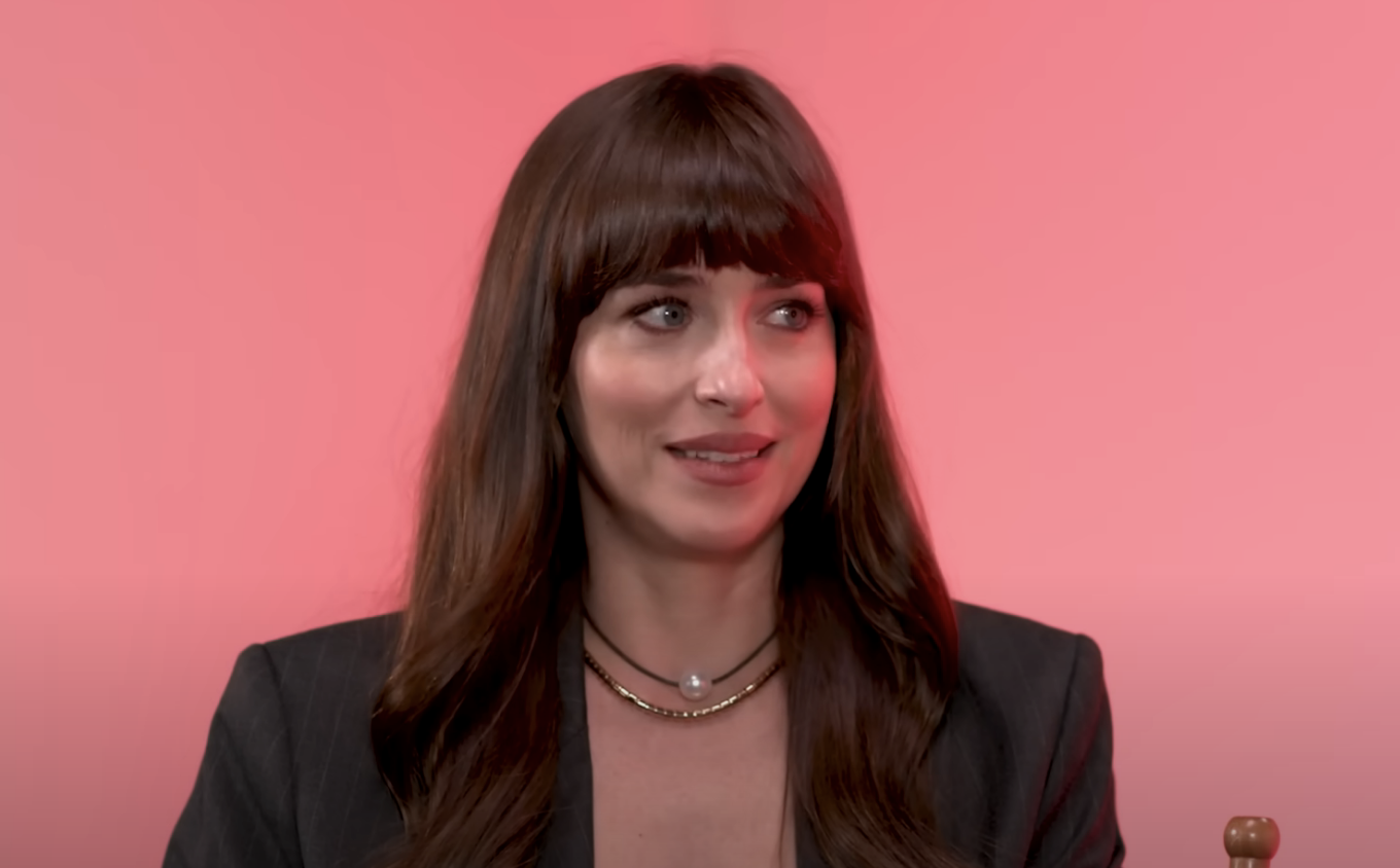 Dakota with a layered necklace, wearing a blazer, smiling in front of a pink background
