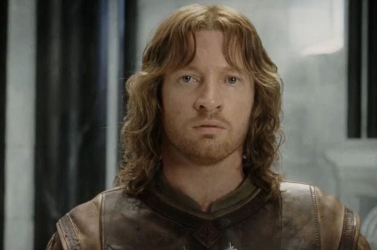 A man with shoulder-length wavy hair and medieval armor looks intently forward