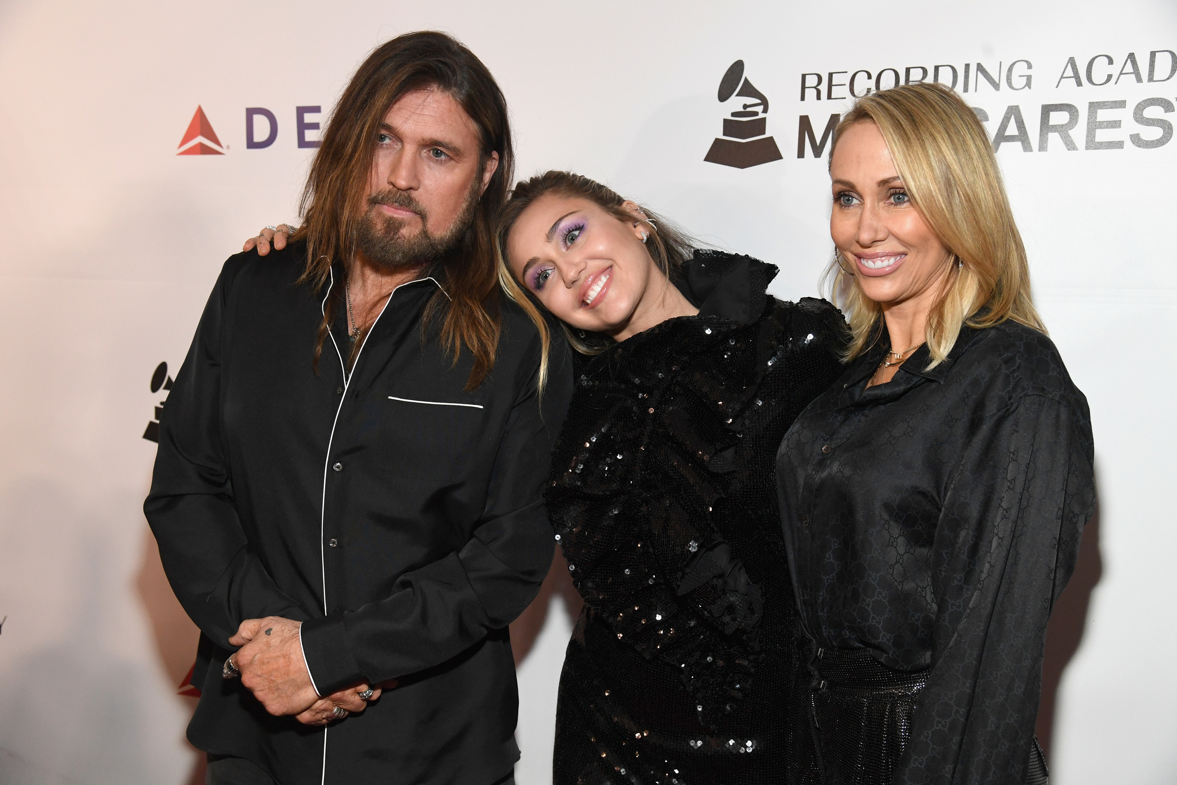 Billy Ray Cyrus, Miley Cyrus, and Tish Cyrus pose together at an event; Miley wears a sparkling black outfit