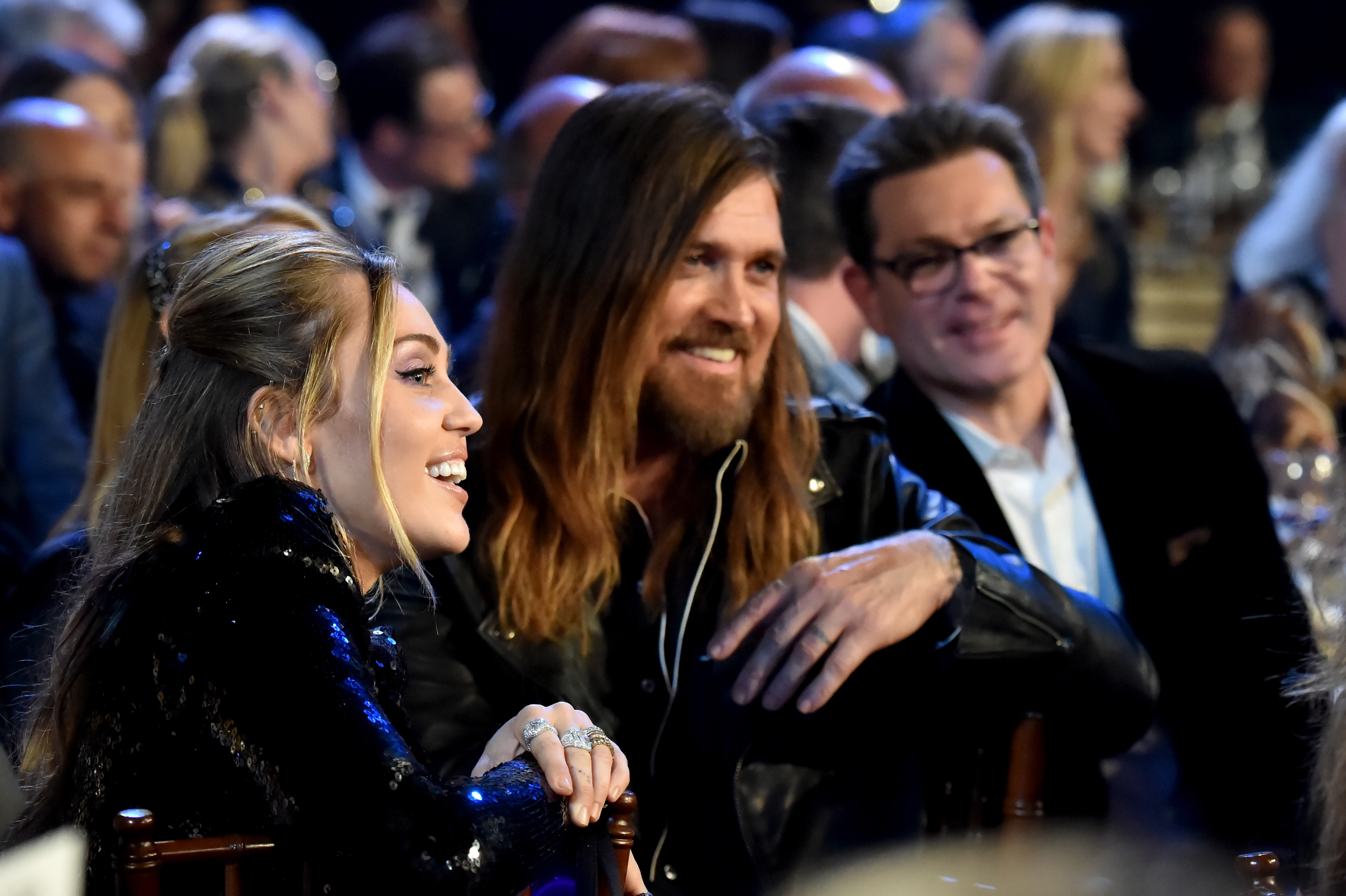 Miley Cyrus and Billy Ray Cyrus seated at an event, smiling and enjoying the moment together