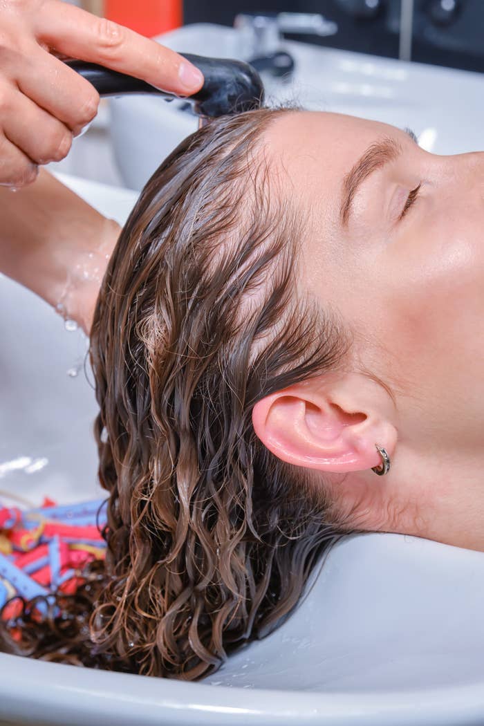 Person getting their hair washed at a salon, head leaning back in a basin, eyes closed