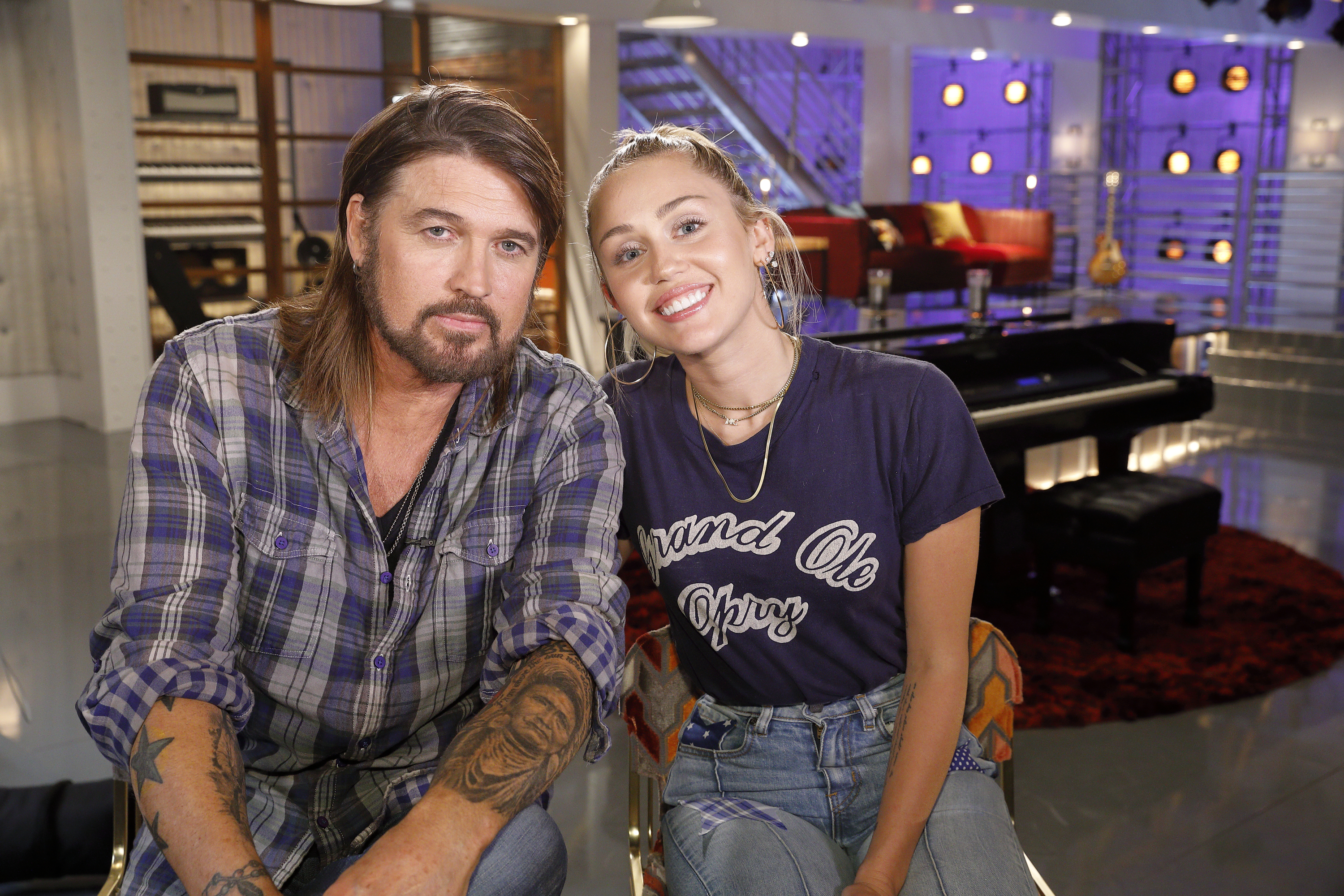 Billy Ray Cyrus and Miley Cyrus sitting together, smiling in a studio setting