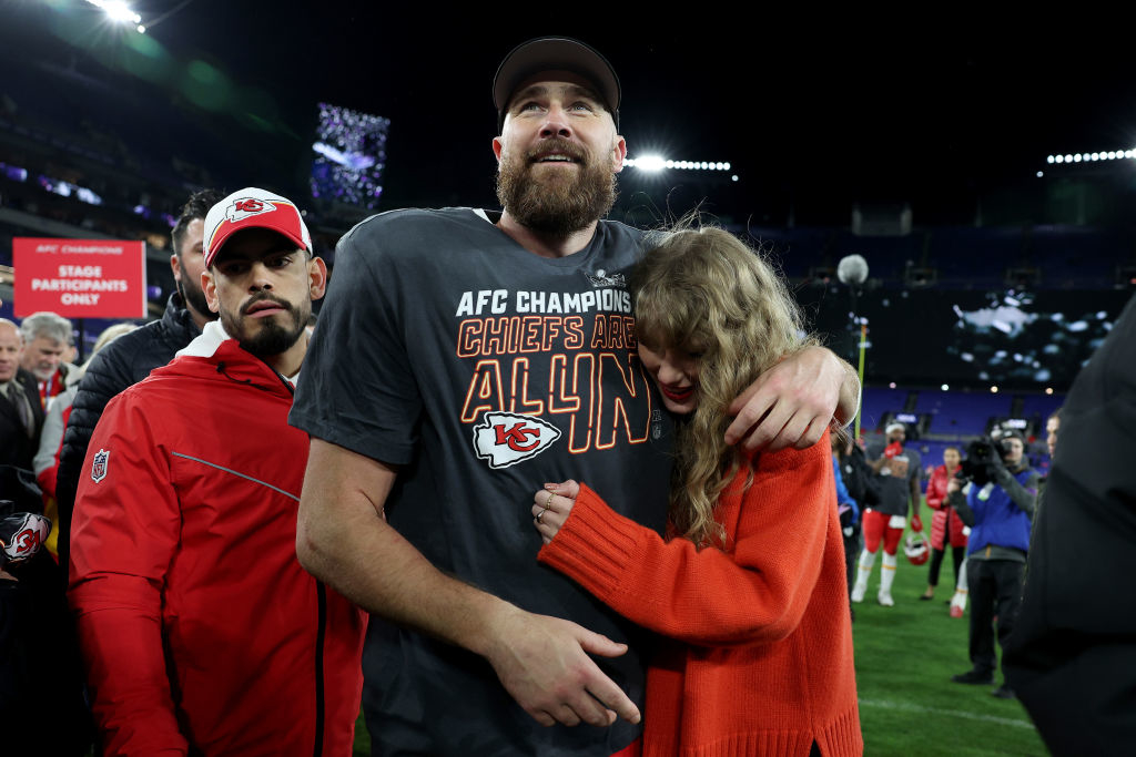 Travis Kelce in a Chiefs t-shirt hugs Taylor, who&#x27;s wearing a big sweater