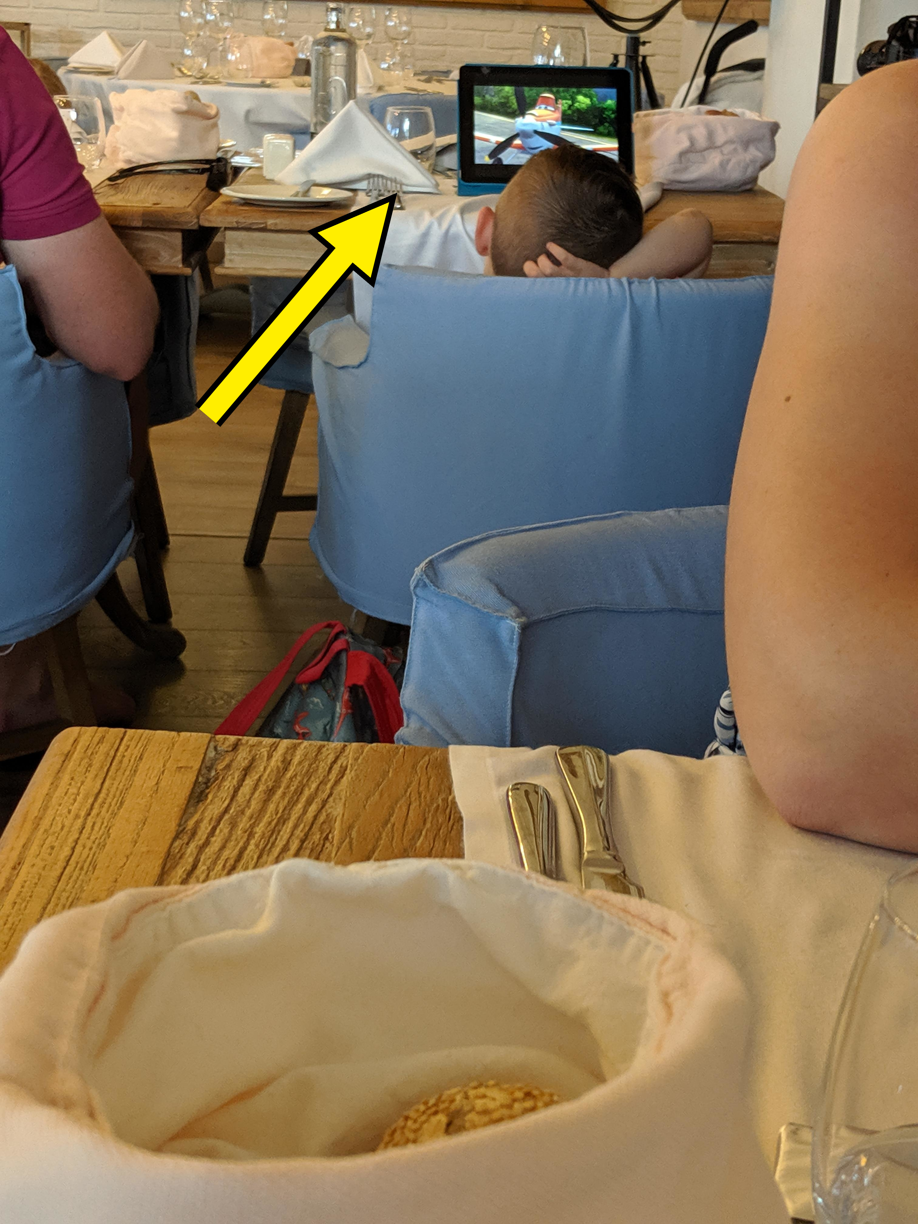Child resting head on table in a restaurant with an iPad playing a movie out loud