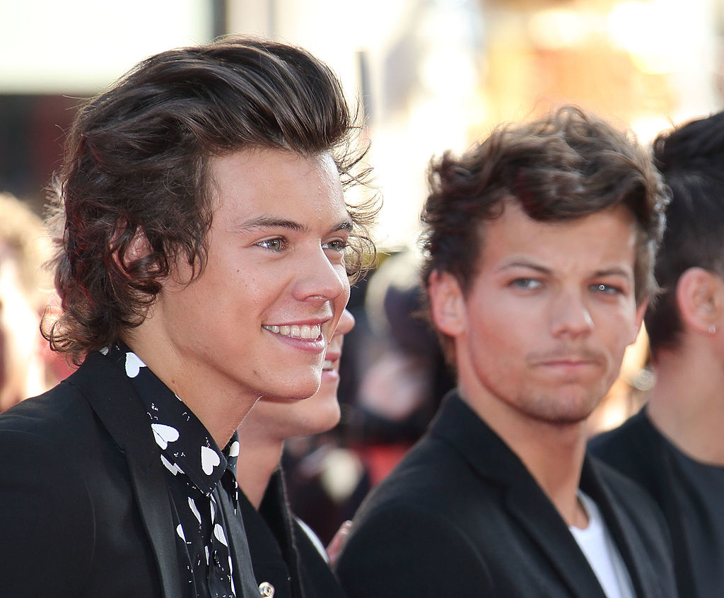 on a red carpet, Louis looks at Harry, who&#x27;s smiling at the camera