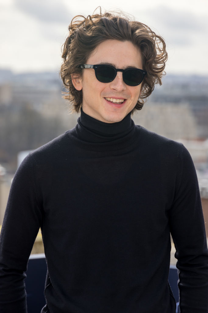 Timothée with wavy hair and sunglasses, wearing a turtleneck, smiling outdoors