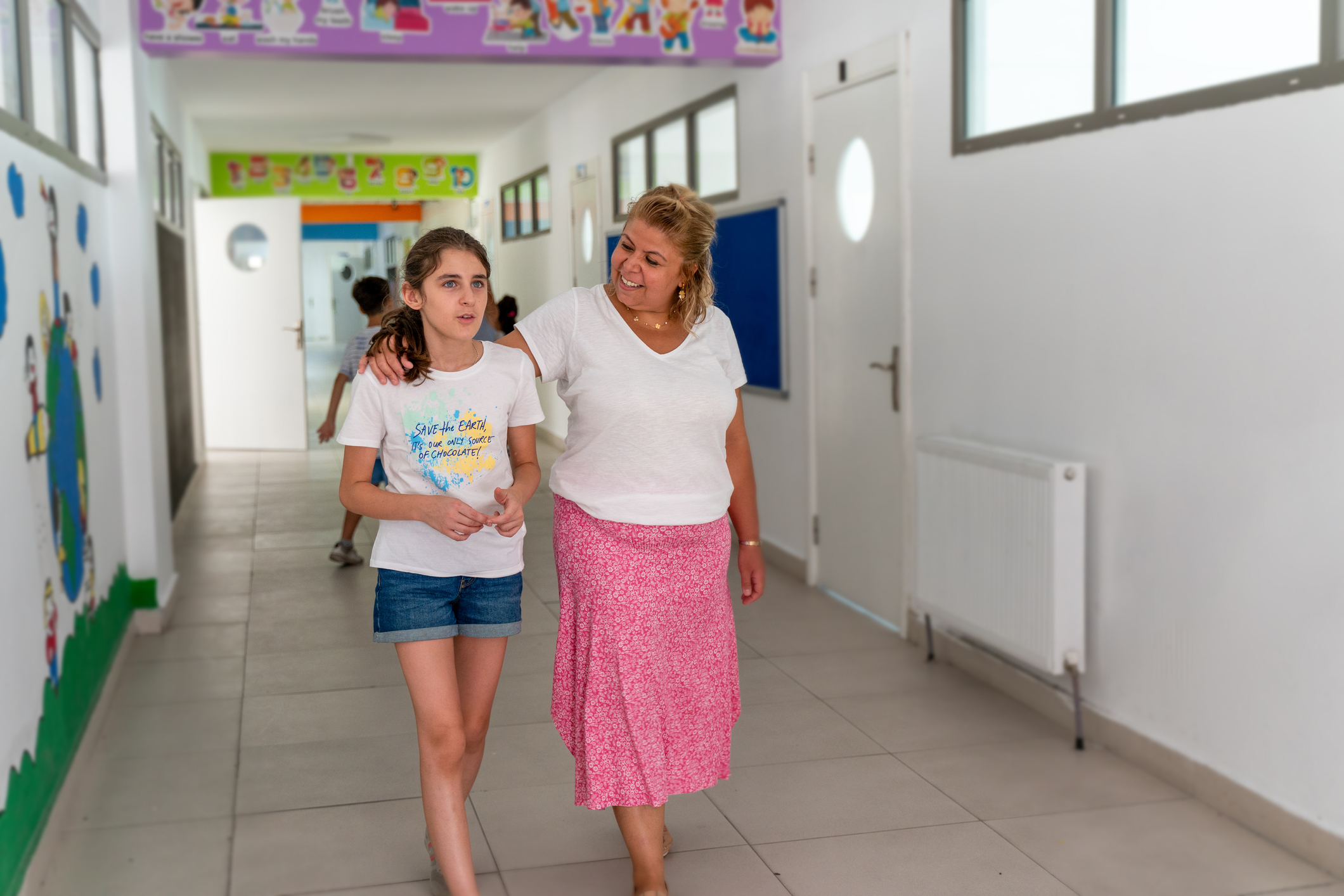 Adult guiding a child through a school hallway, both looking at each other