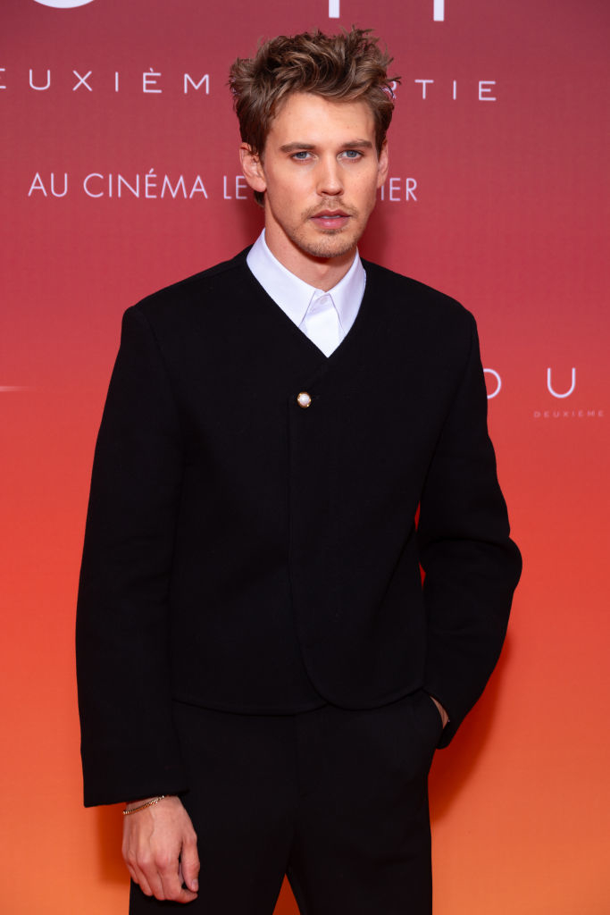 Austin standing on red carpet in black jacket over white shirt, looking ahead