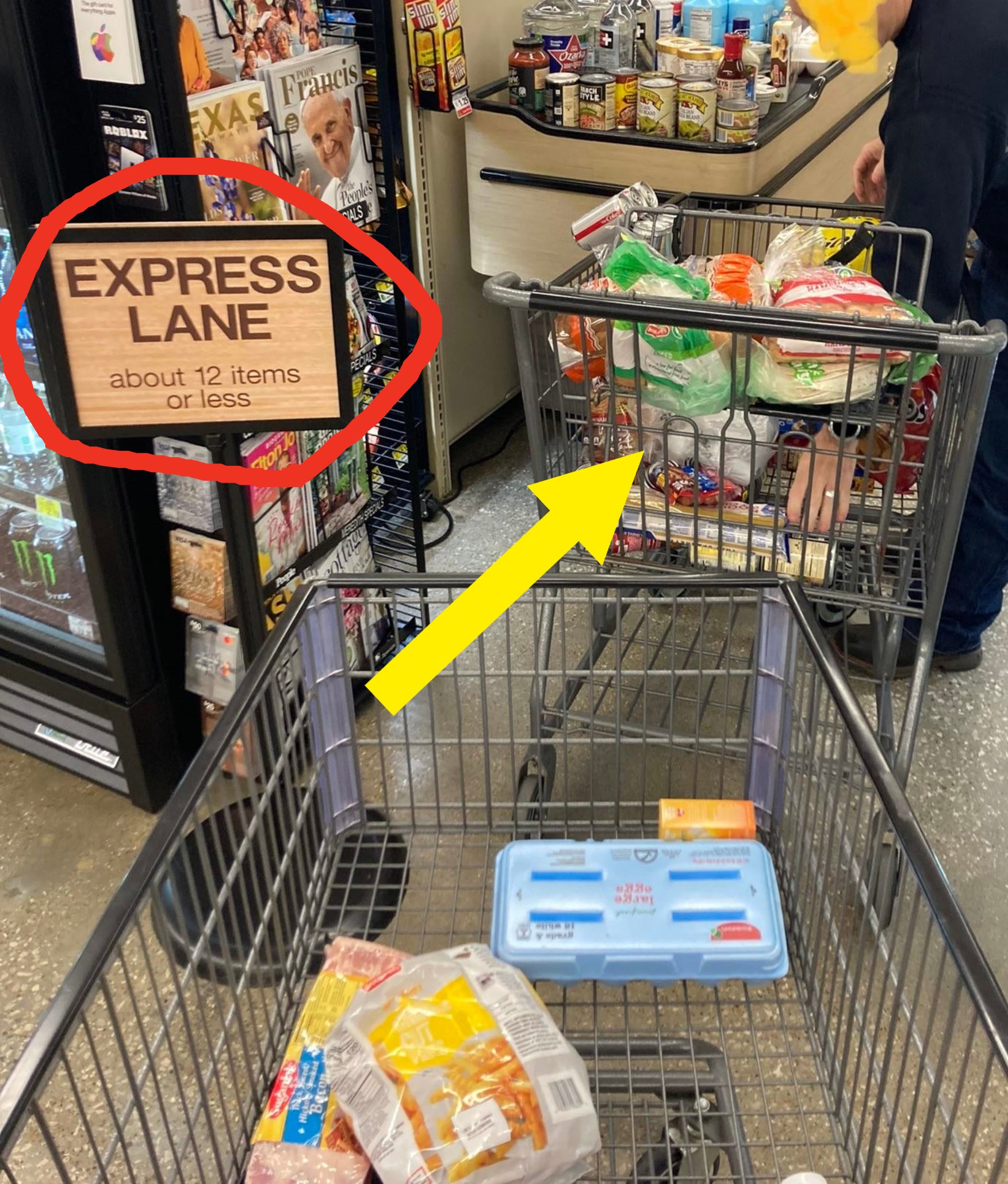 A grocery store express lane with &quot;about 12 items or less&quot; sign. Person checking out with a full cart