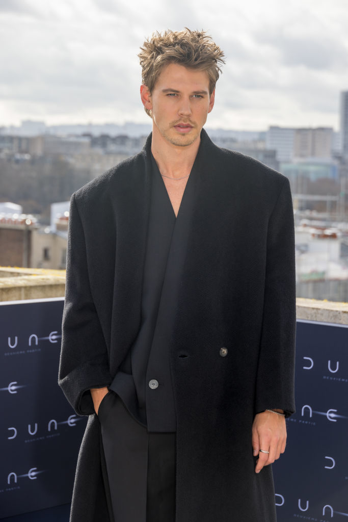 Austin in a stylish black overcoat and suit posing at an outdoor event