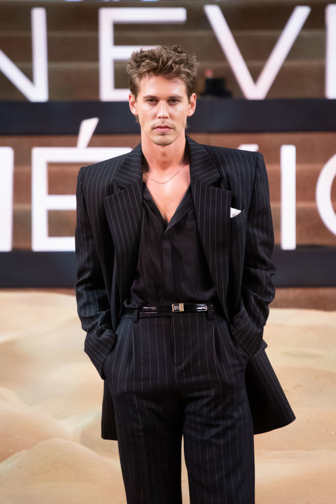 Austin in a pin-striped suit posing with hands in pockets on a stage