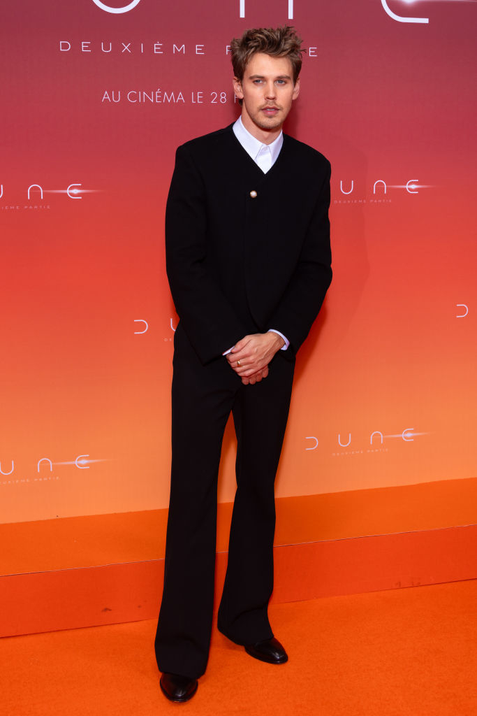 Austin in a black suit standing before an orange backdrop at &quot;Dune&quot; event