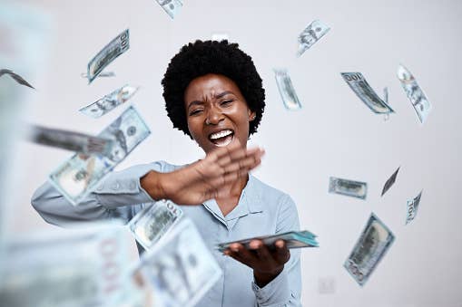 Woman in a blue shirt joyfully throwing money into the air
