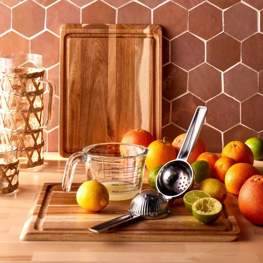 Various kitchenware including a measuring cup, juicer, and cutting boards displayed with citrus fruits on a countertop
