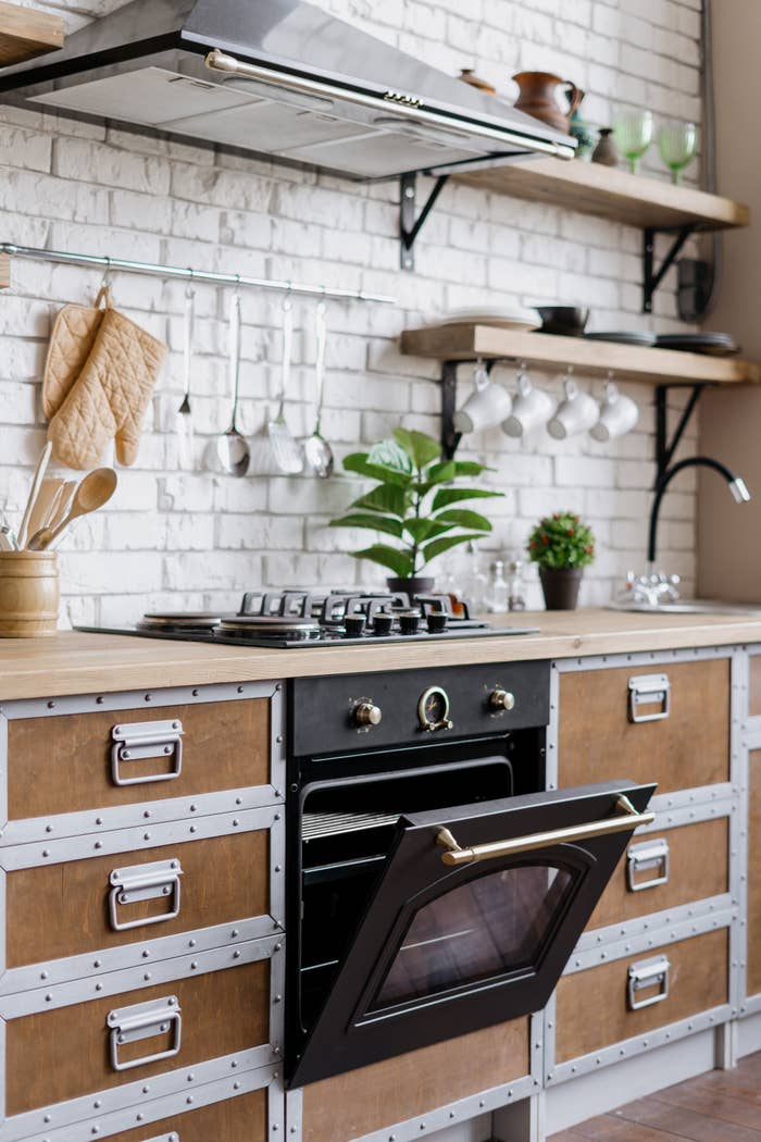 Modern kitchen with open oven door, gas stove, and metal-trimmed storage drawers with open shelving