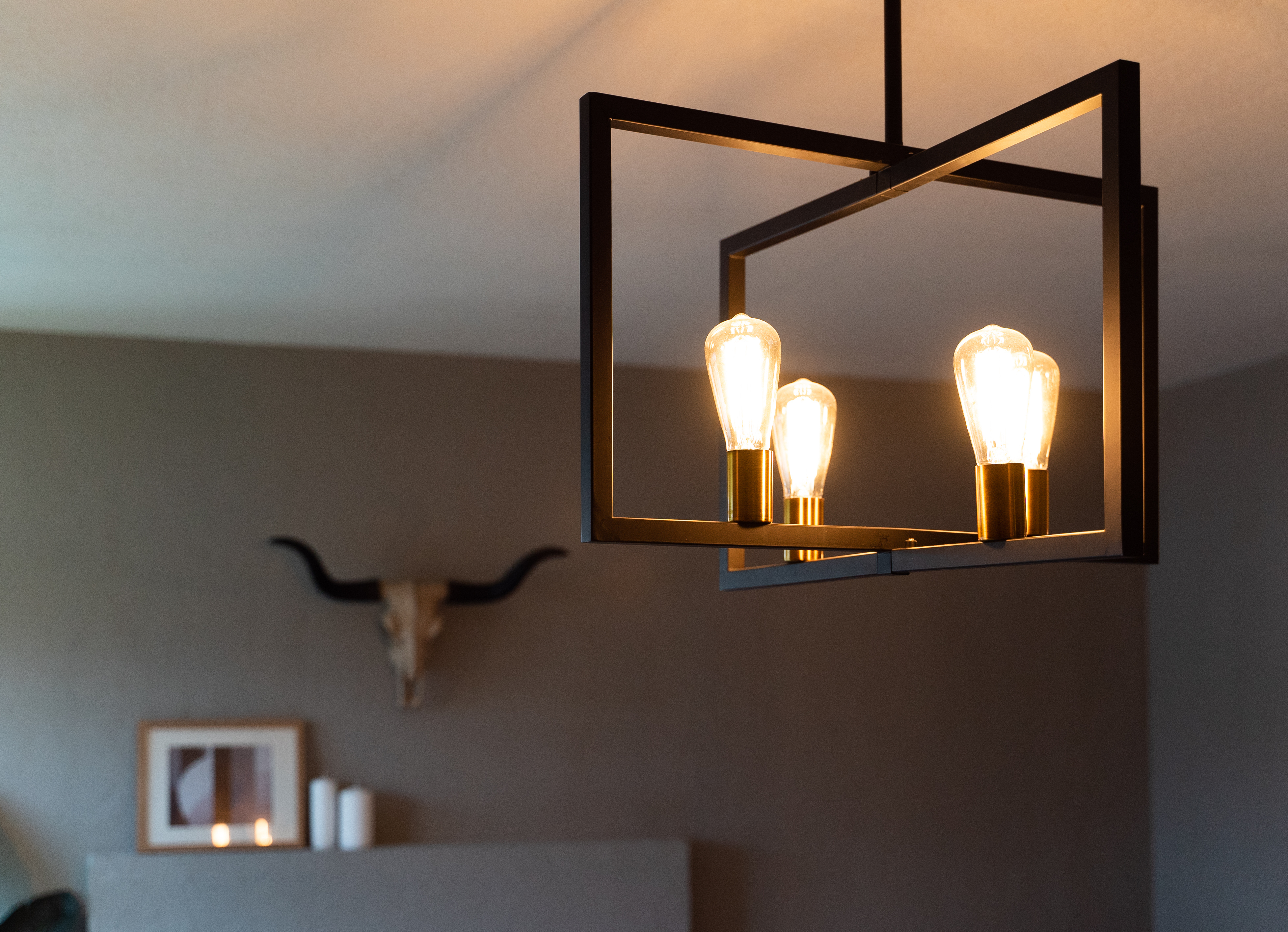 Modern chandelier with exposed bulbs hanging in a room, below a wall-mounted animal skull decor