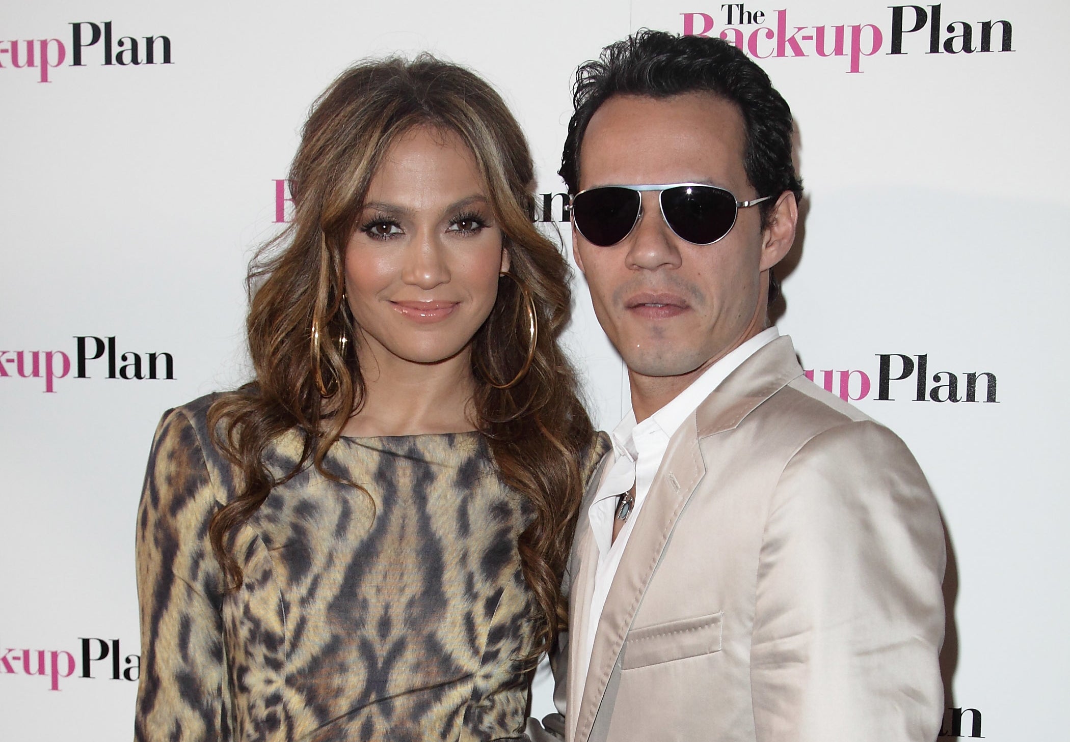 Jennifer Lopez in a leopard print dress and Marc Anthony in a beige suit pose together at an event