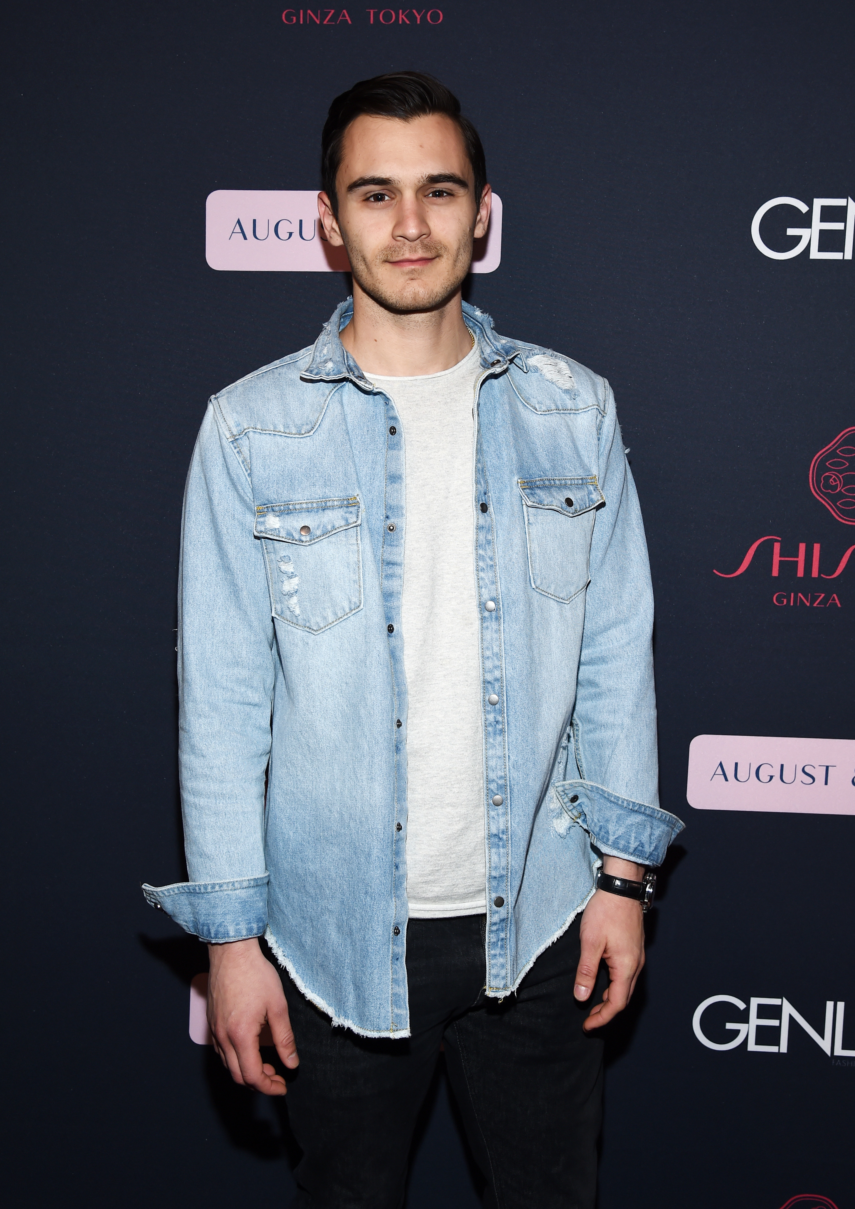 Man in a denim jacket over a shirt, standing on a branded backdrop