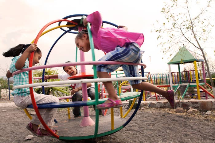 Three children play on a circular jungle gym at a playground