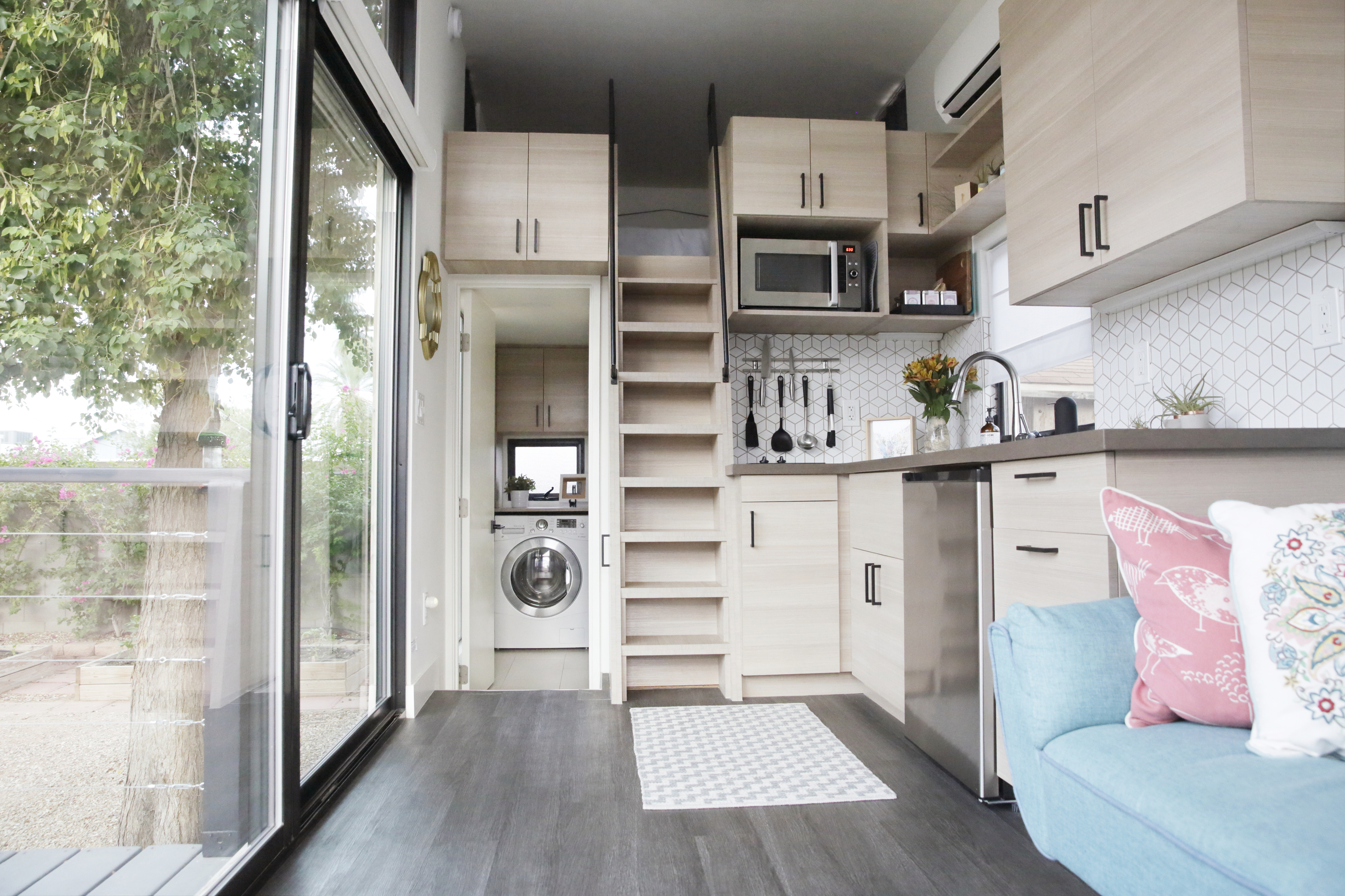 Two-level tiny home interior with kitchen, staircase, and seating area with a gray floor