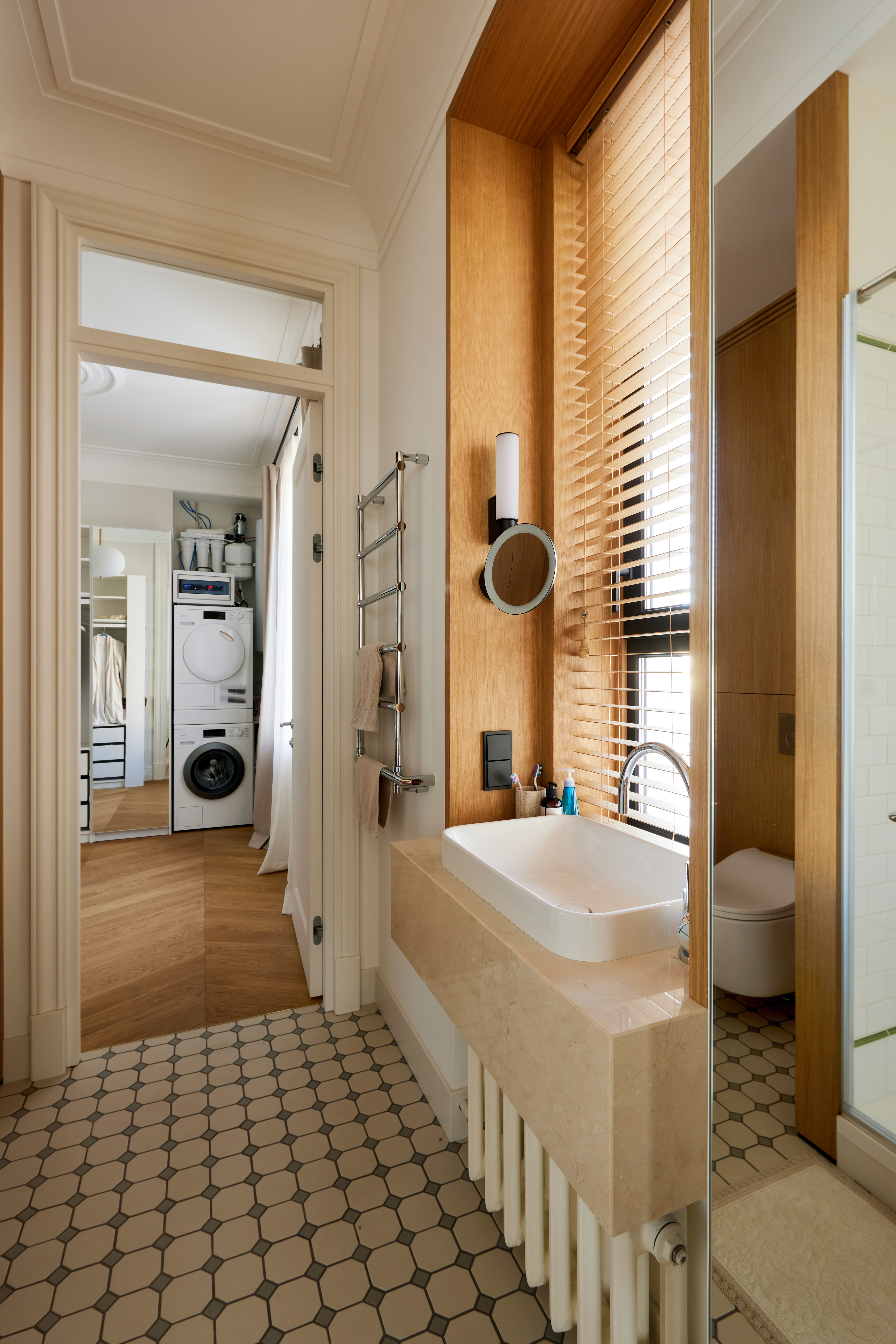 A bathroom with a sink and mirror opens to a view of a laundry room and closet