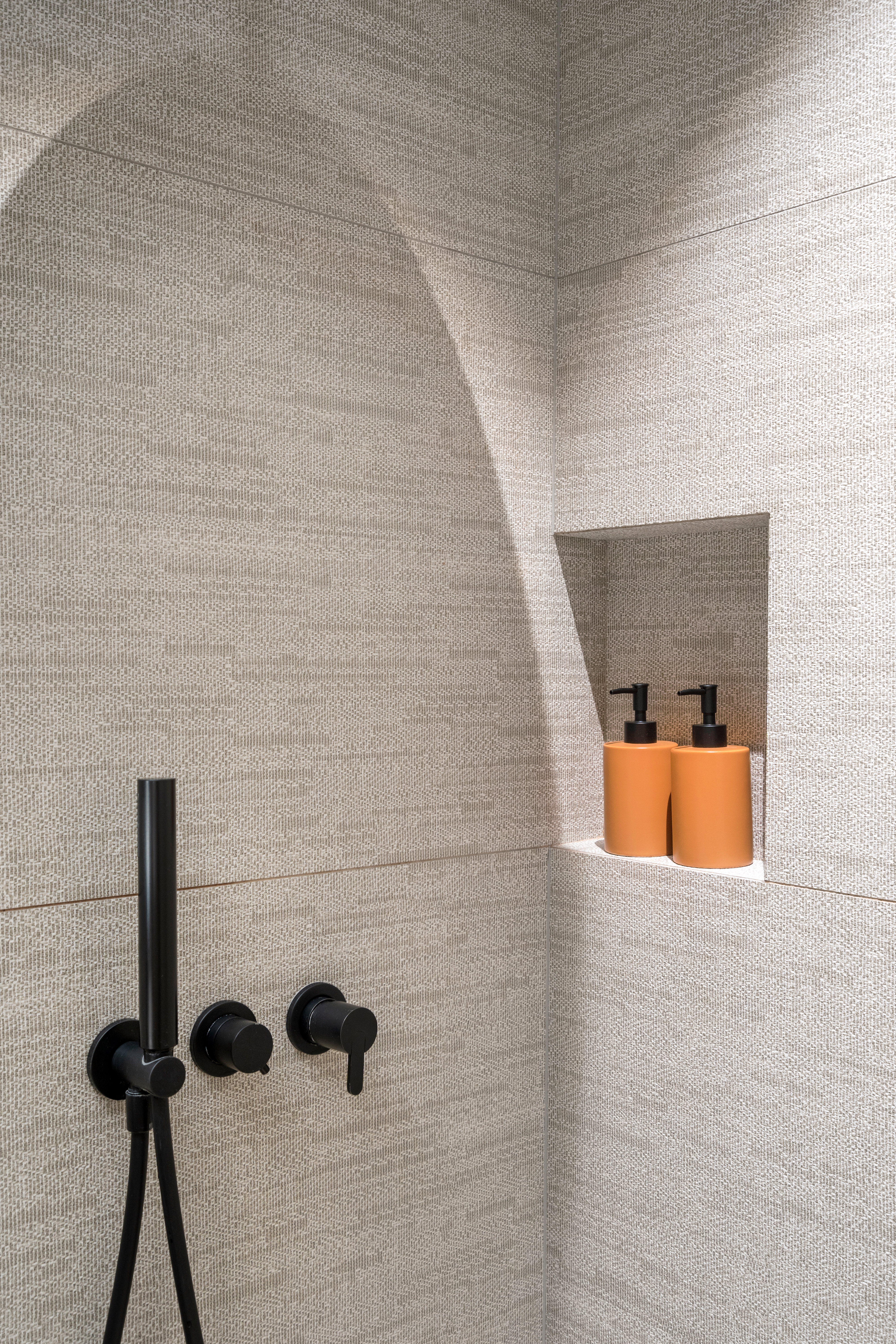 A modern shower corner with a minimalist black faucet and niche for toiletries