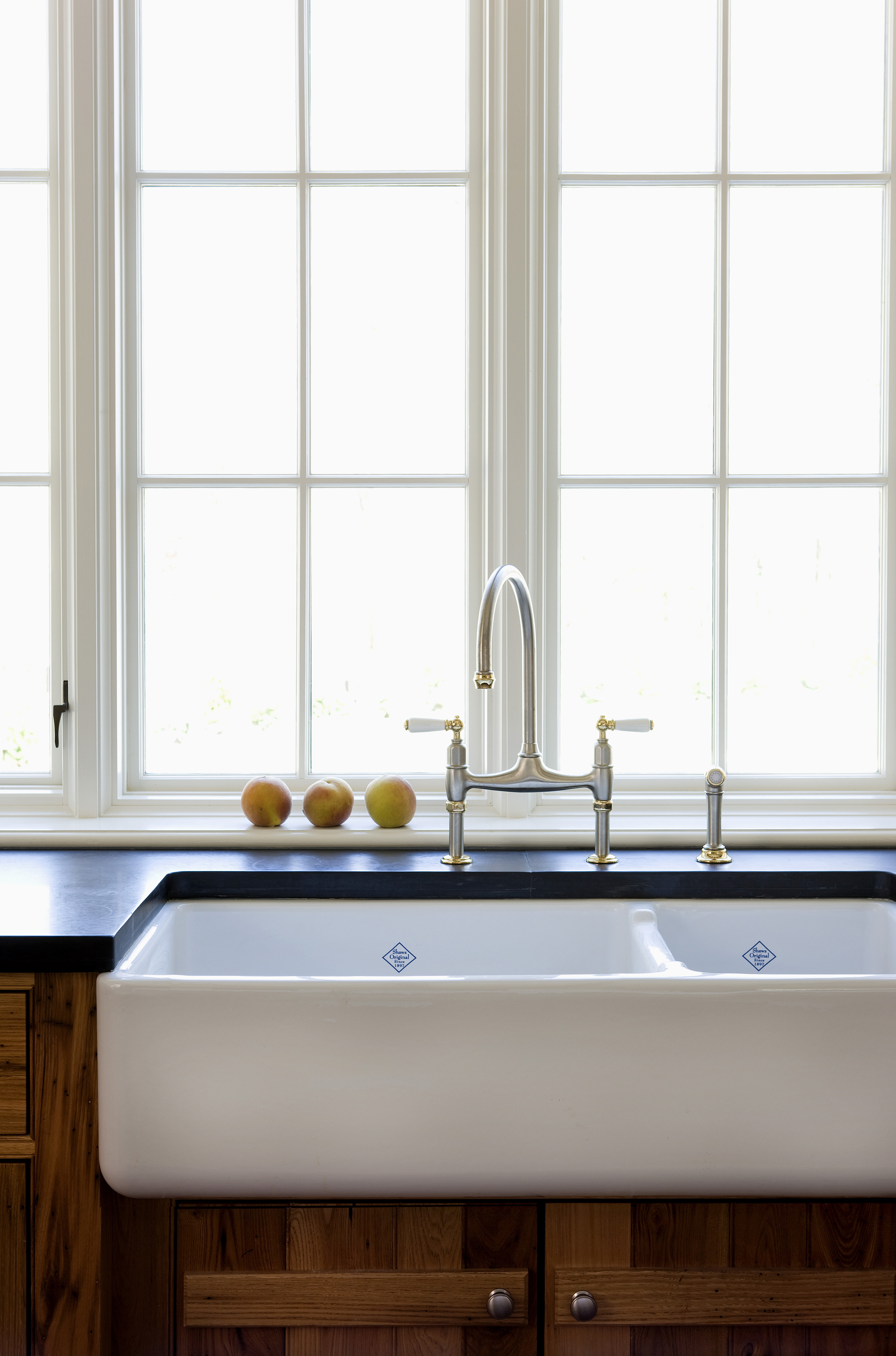 A farmhouse-style kitchen sink with a modern faucet set in front of a window, flanked by wooden cabinets