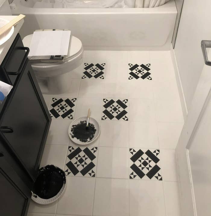 A bathroom floor with someone doing a paint touch-up next to a toilet and waste bin