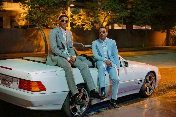 Two individuals in suits seated on the trunk of a luxury car at night