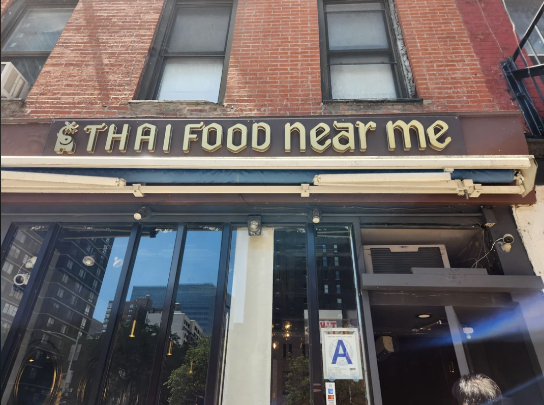 Sign reads &quot;$ THAI Food near me&quot; above a restaurant entrance with a grade A health rating