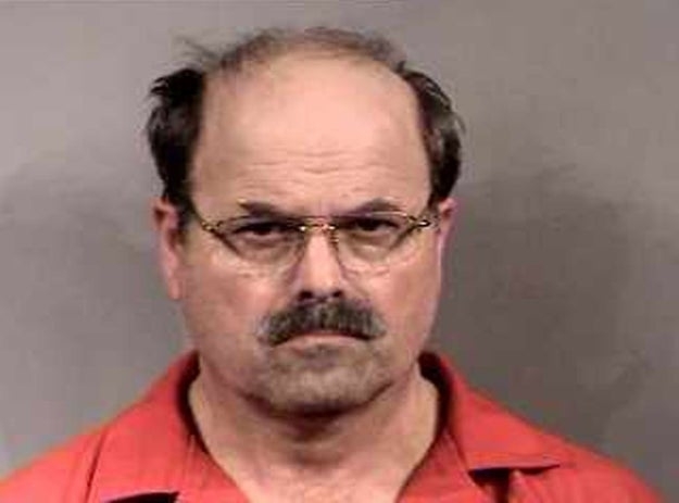 Rader, with a mustache, in orange attire and glasses looking at the camera