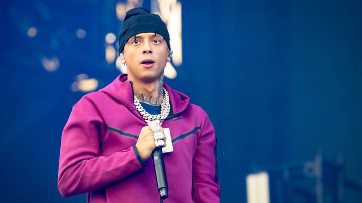Central Cee wearing a beanie and a pink hoodie holding a microphone on stage