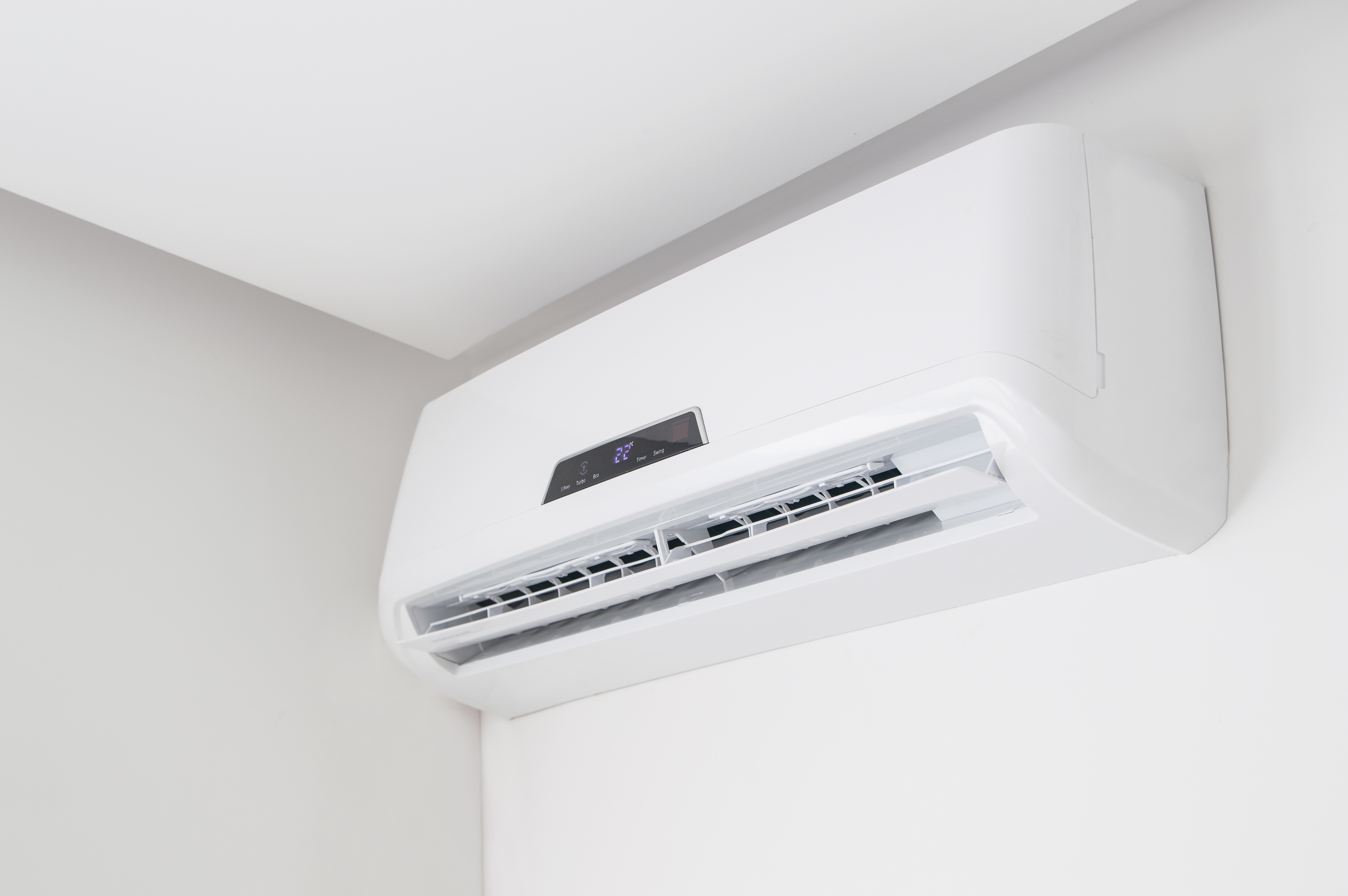 Wall-mounted air conditioning unit with a digital display, installed in a corner near the ceiling