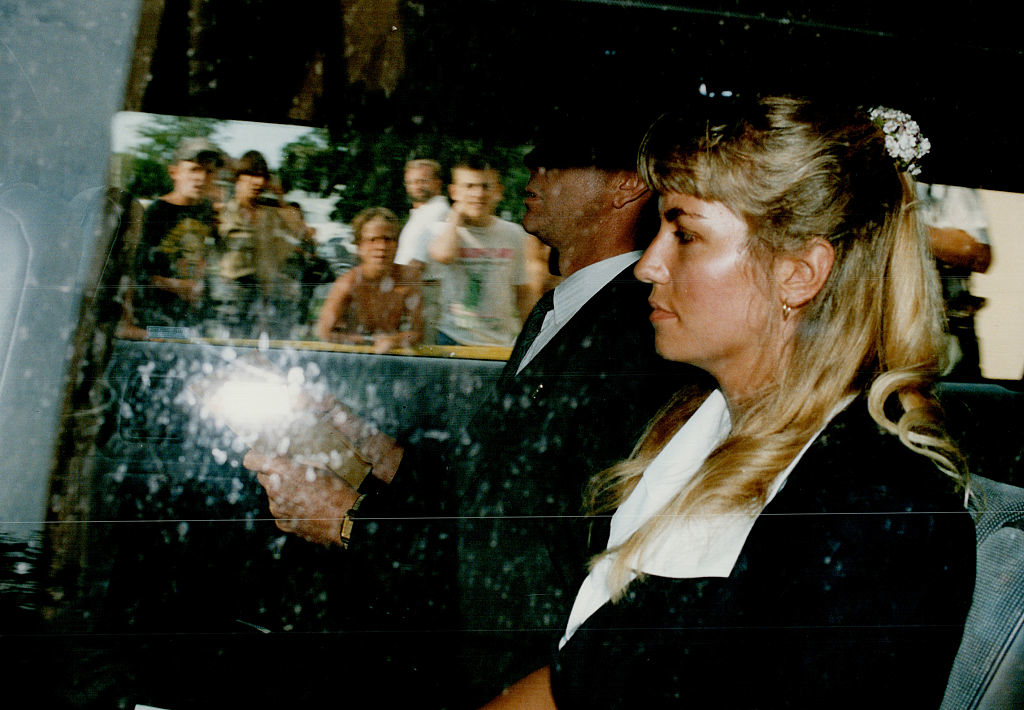 Paul with a woman in a car, viewed through a window with reflections