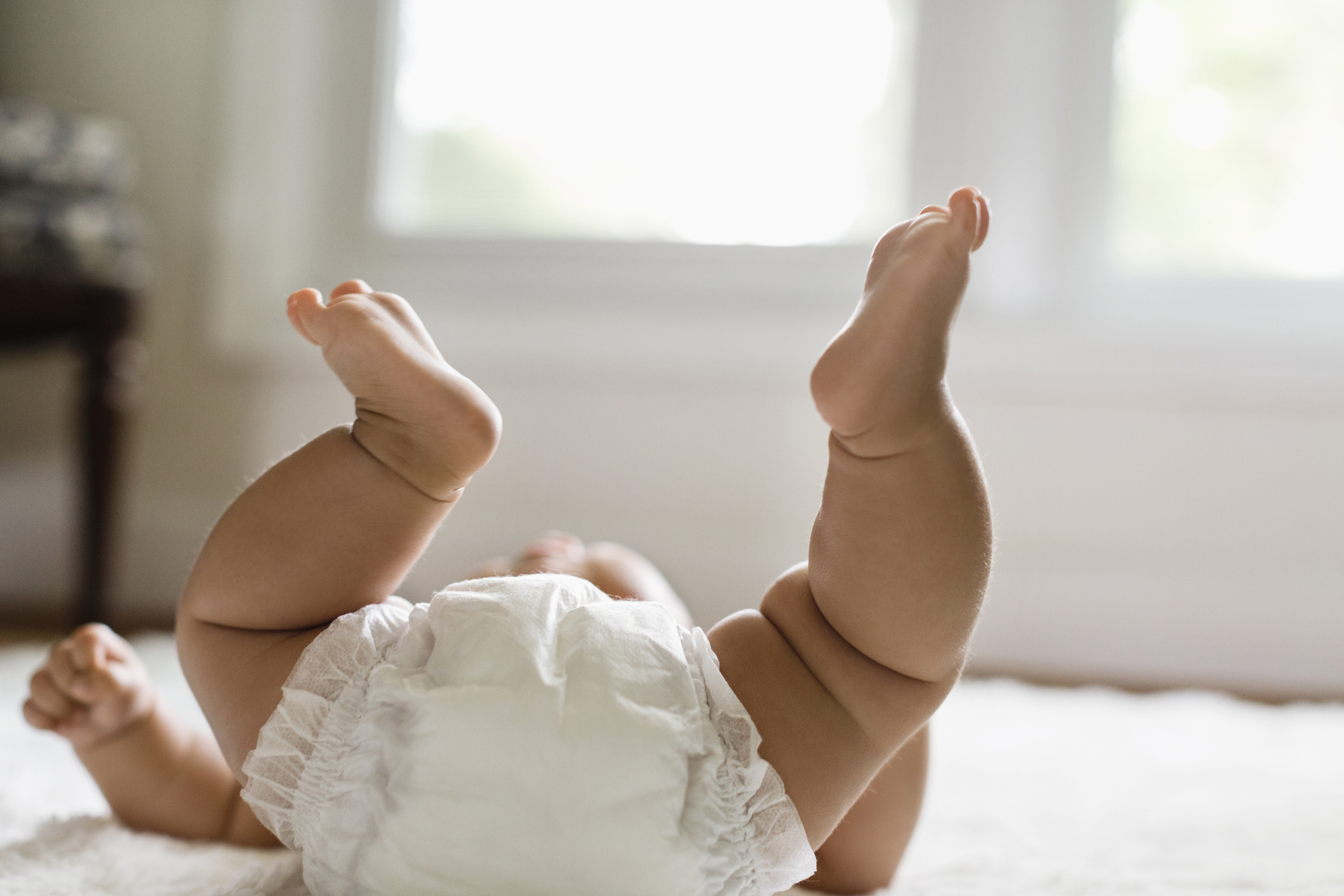 Baby lying on their stomach lifting legs up, in a white diaper, on a soft surface, capturing a playful moment