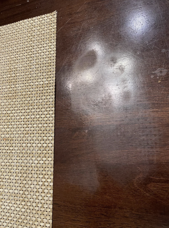 Imprint of a child's face on a wooden table next to a woven placemat